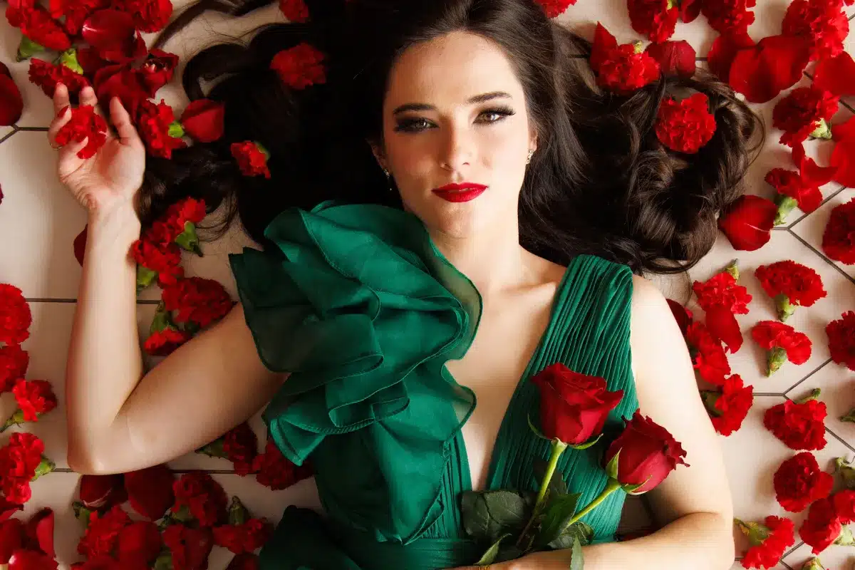 A woman lies on a bed, surrounded by vibrant red roses, creating a romantic and serene atmosphere.