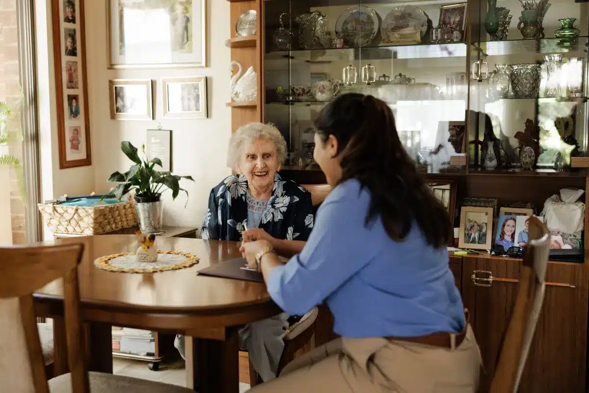 A woman and an older woman sit together at a table, engaged in conversation and sharing a moment.