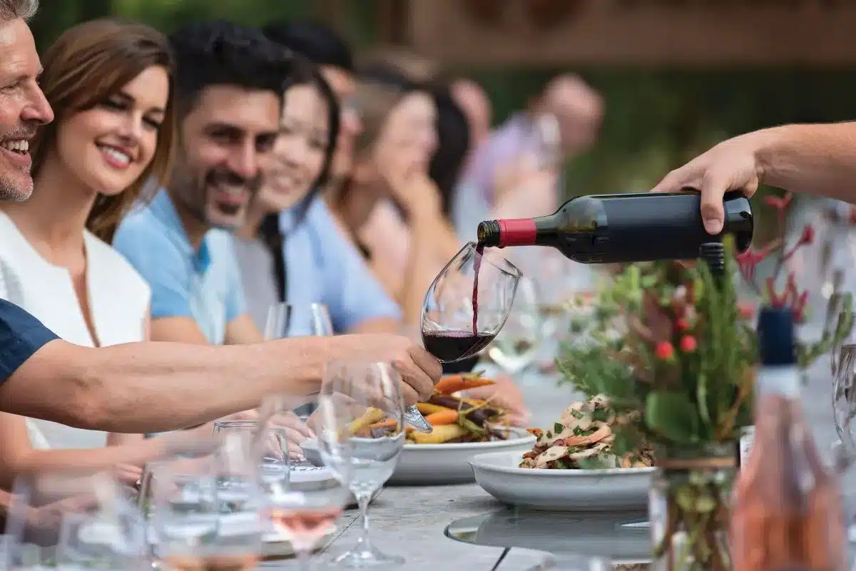 A group of people enjoying a meal together at a table, each with a wine glass in hand, engaged in conversation.