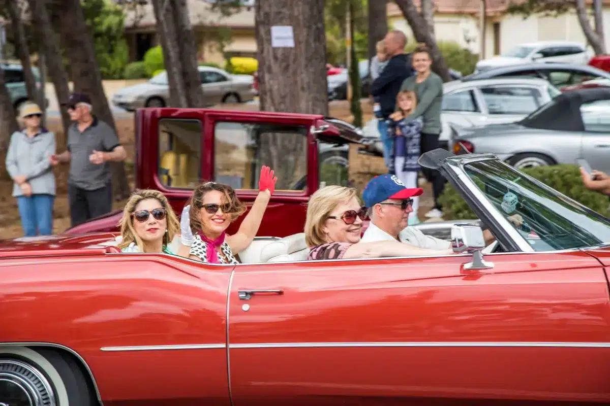 A group of people in a convertible car happily waving at the camera.