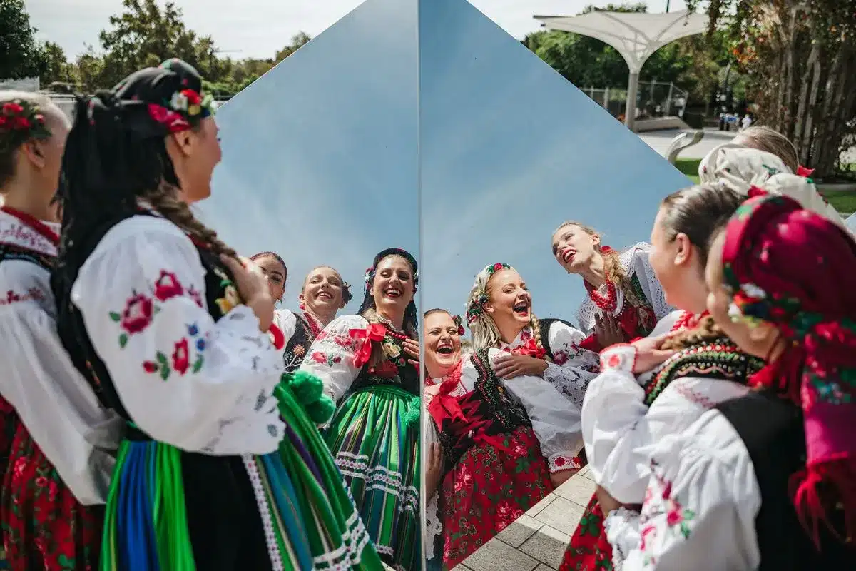 Women in traditional costumes admire their reflections in a mirror.