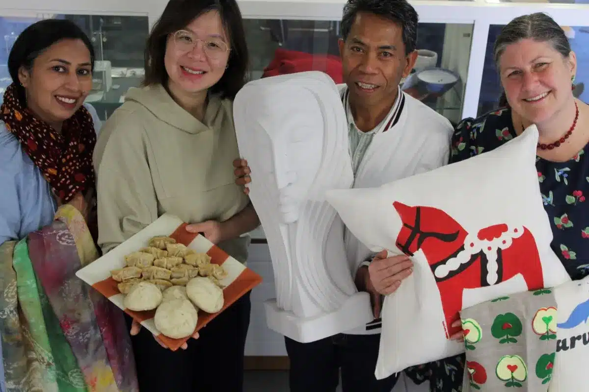 Four people joyfully holding up colorful pillows and various food items in a cheerful setting.