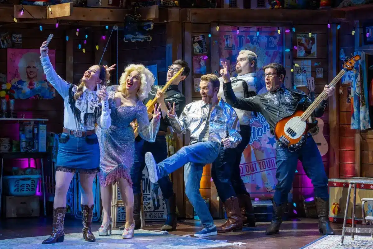 A musical cast captivates the audience on stage, displaying a variety of costumes, instruments and synchronized dance moves.