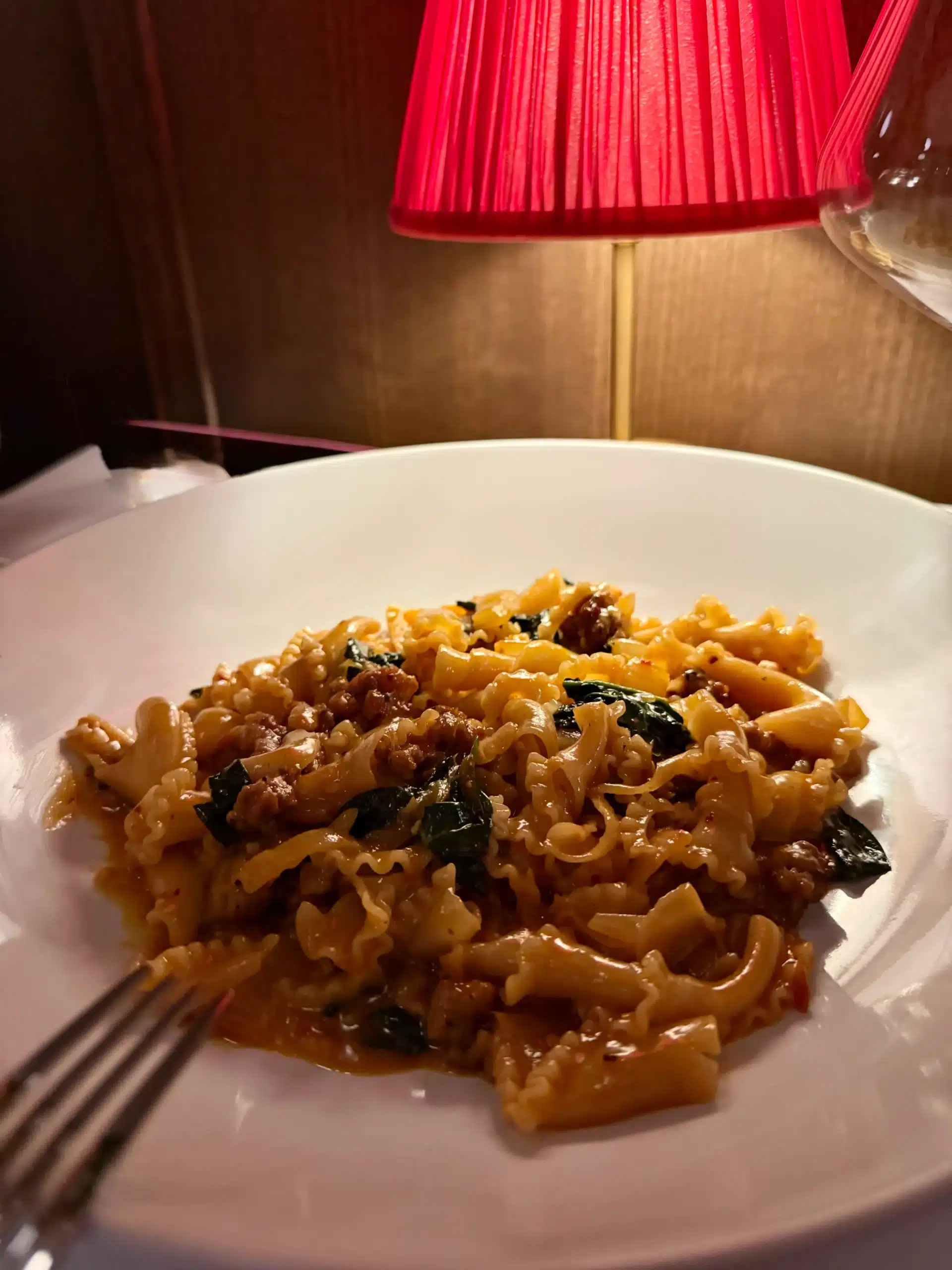 A bowl of pasta topped with a rich, dark sauce and grated cheese, placed on a wooden dining table.