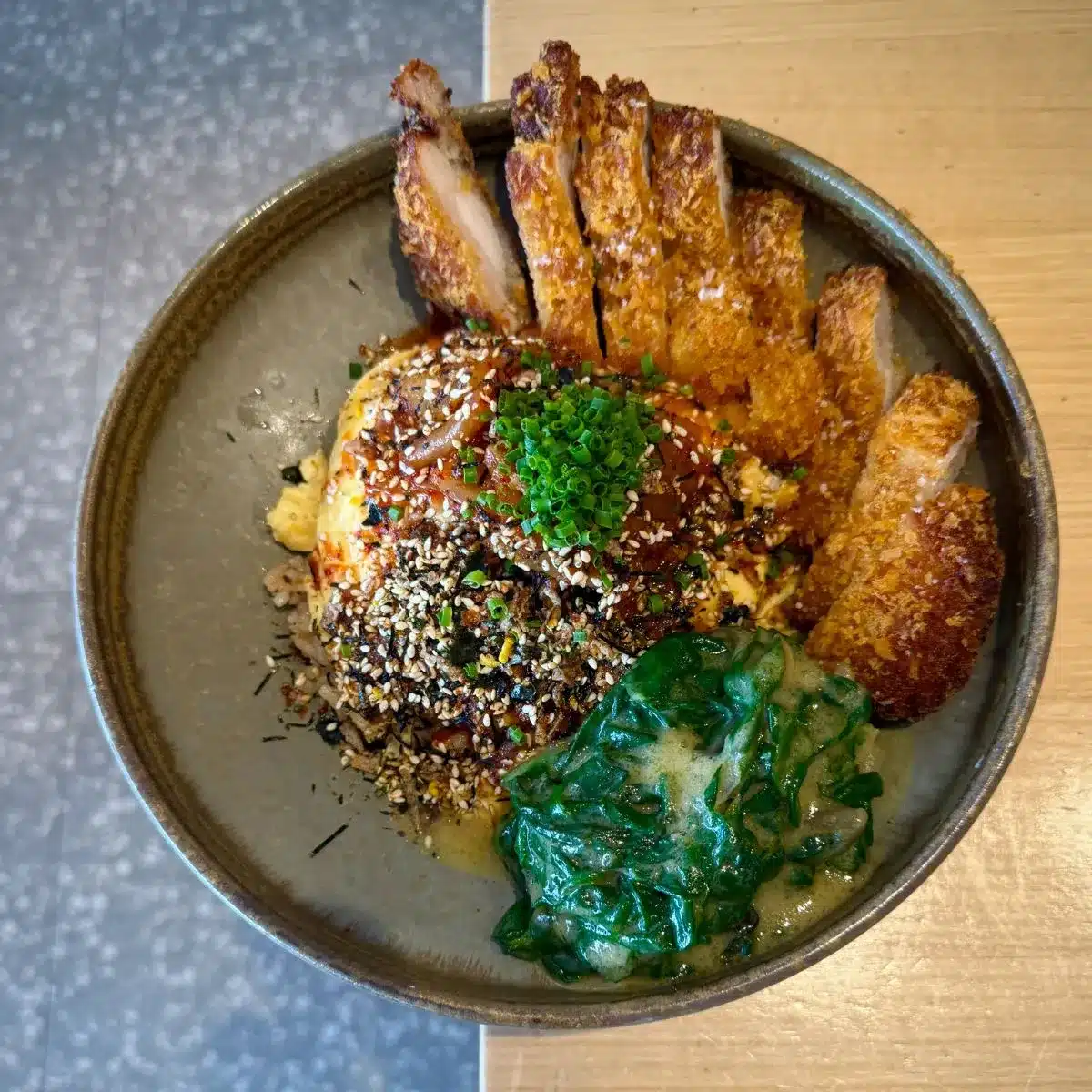A bowl of fried chicken served over rice with kimchi, furikake, and spring onions, photographed from above.