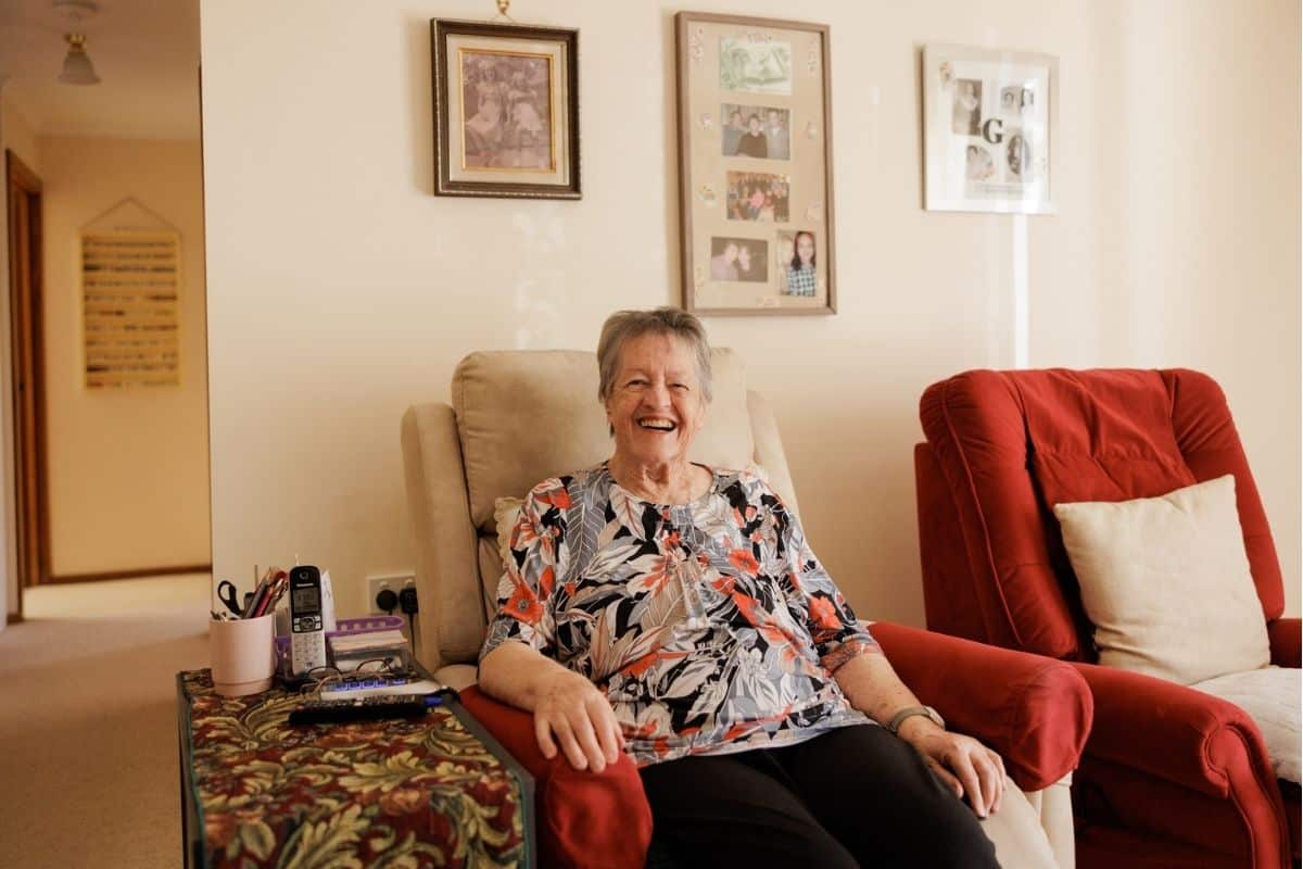 An elderly woman relaxed in a chair within her living room, featuring inviting furnishings and a homely atmosphere.