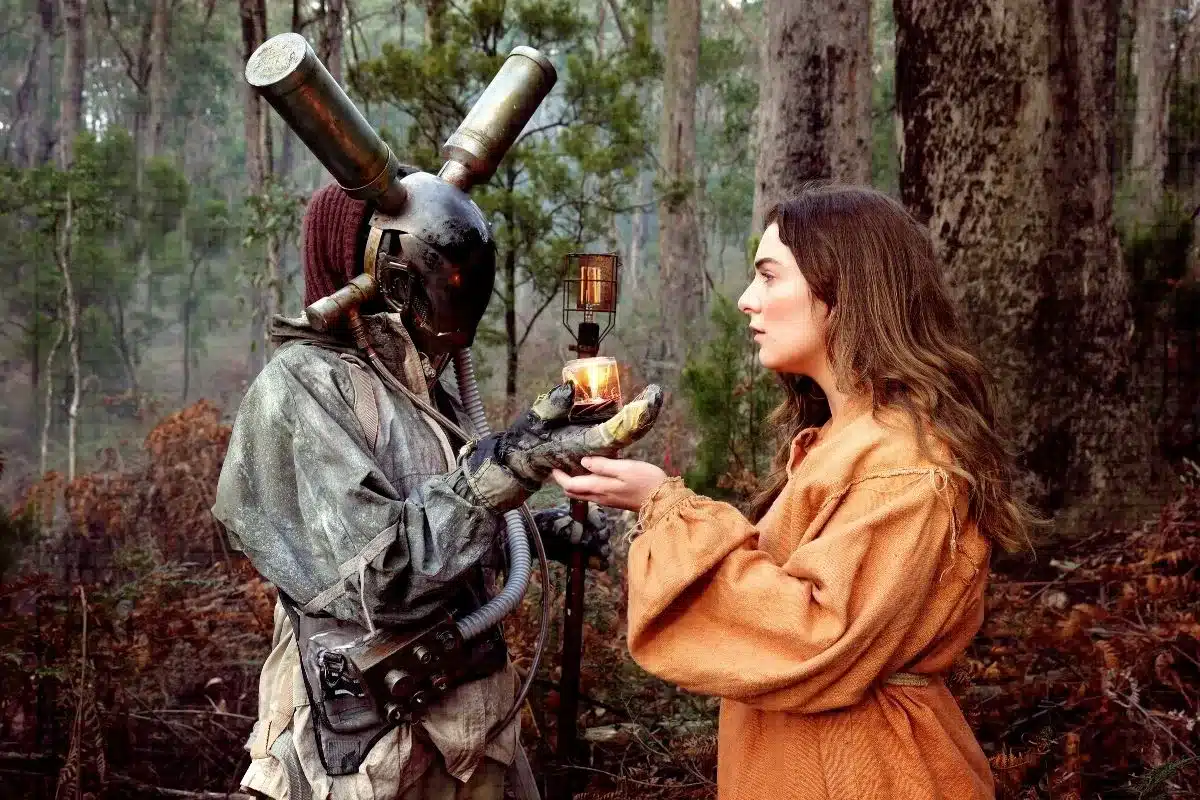 A woman in a costume offers an apple to a man in a costume, both engaged in a playful exchange advertising poster for A Concise Compendium of Wonder