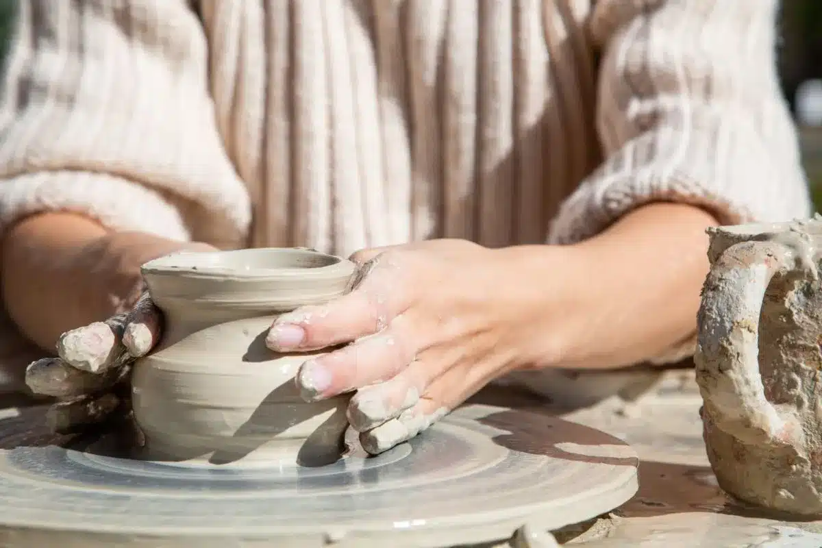 A woman shapes a clay pot on a potter's wheel, focused on her craft in a well-lit pottery studio.