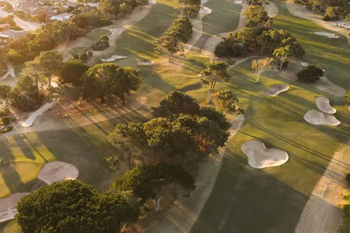 Aerial view of a lush golf course featuring manicured grass and scattered trees under a clear blue sky.