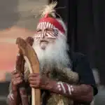Elderly man with a long white beard, wearing a thoughtful expression and traditional Aboriginal clothing.