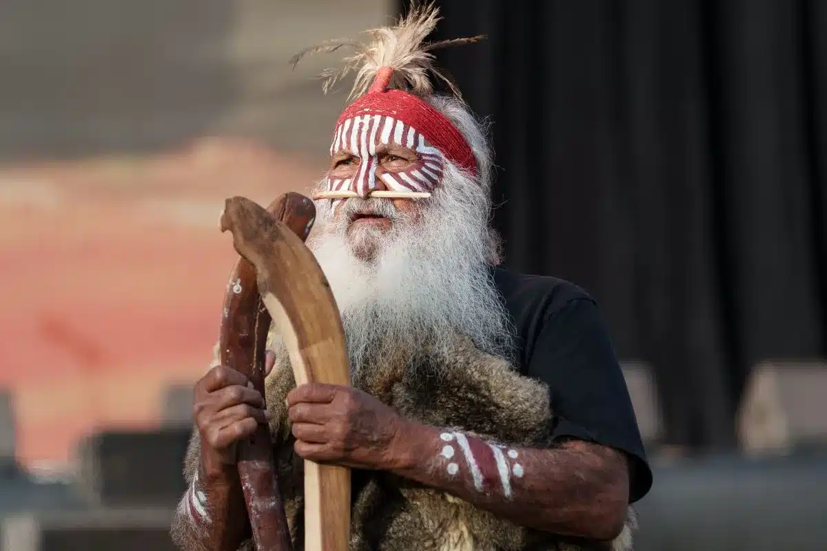 Elderly man with a long white beard, wearing a thoughtful expression and traditional Aboriginal clothing.