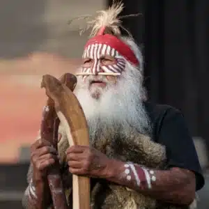 Elderly man with a long white beard, wearing a thoughtful expression and traditional Aboriginal clothing.