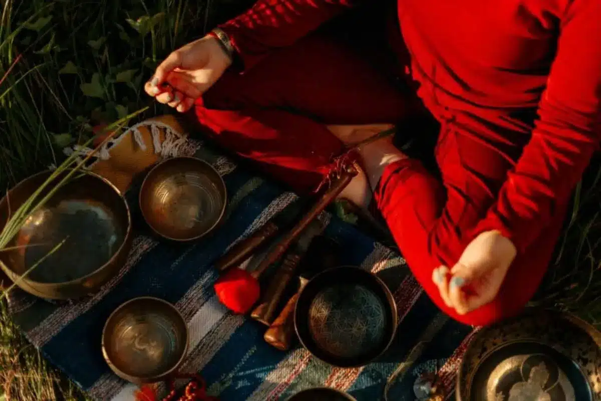 A woman in red sits in meditation on the ground with crossed legs with a holistic offering in front of her