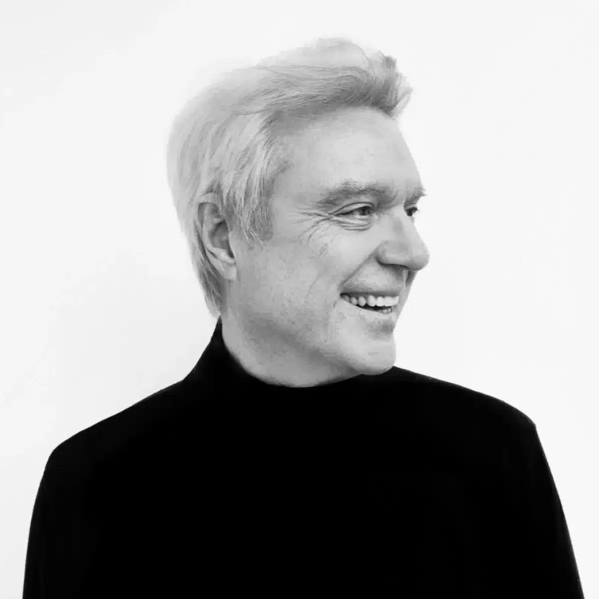 Black and white portrait of musician David Byrne looking out into the distance and smiling