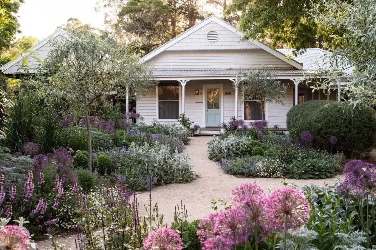 A serene garden showcasing purple flowers with a white house nestled in the background.