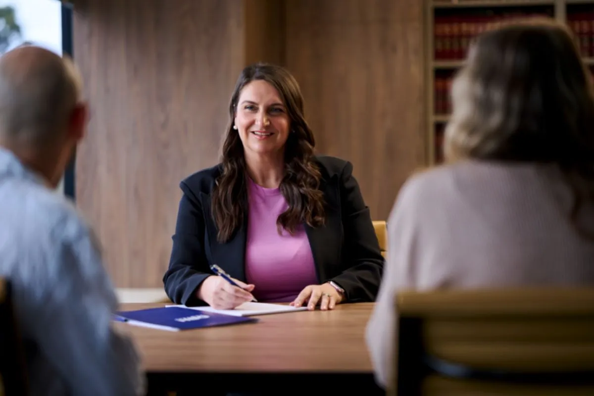 A lawyer smiles at their client with legal pad during a consultation. 