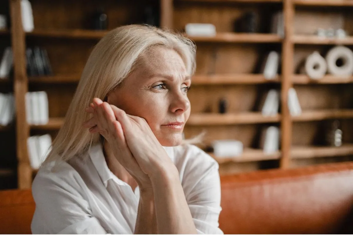 A middle aged woman looks contemplatively into the distance in a home setting.