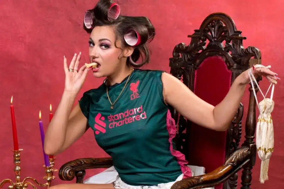 A woman poses in on a throne with hair curlers in a brightly coloured room