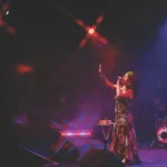 A woman performs in costume to a captivated audience under bright stage lights.