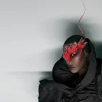 Grace Jones dressed in a lavish coat and red face mask.