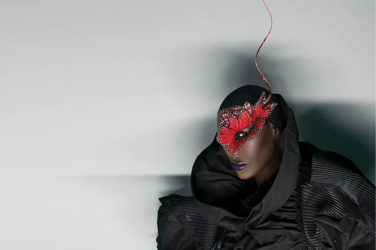 Grace Jones dressed in a lavish coat and red face mask.