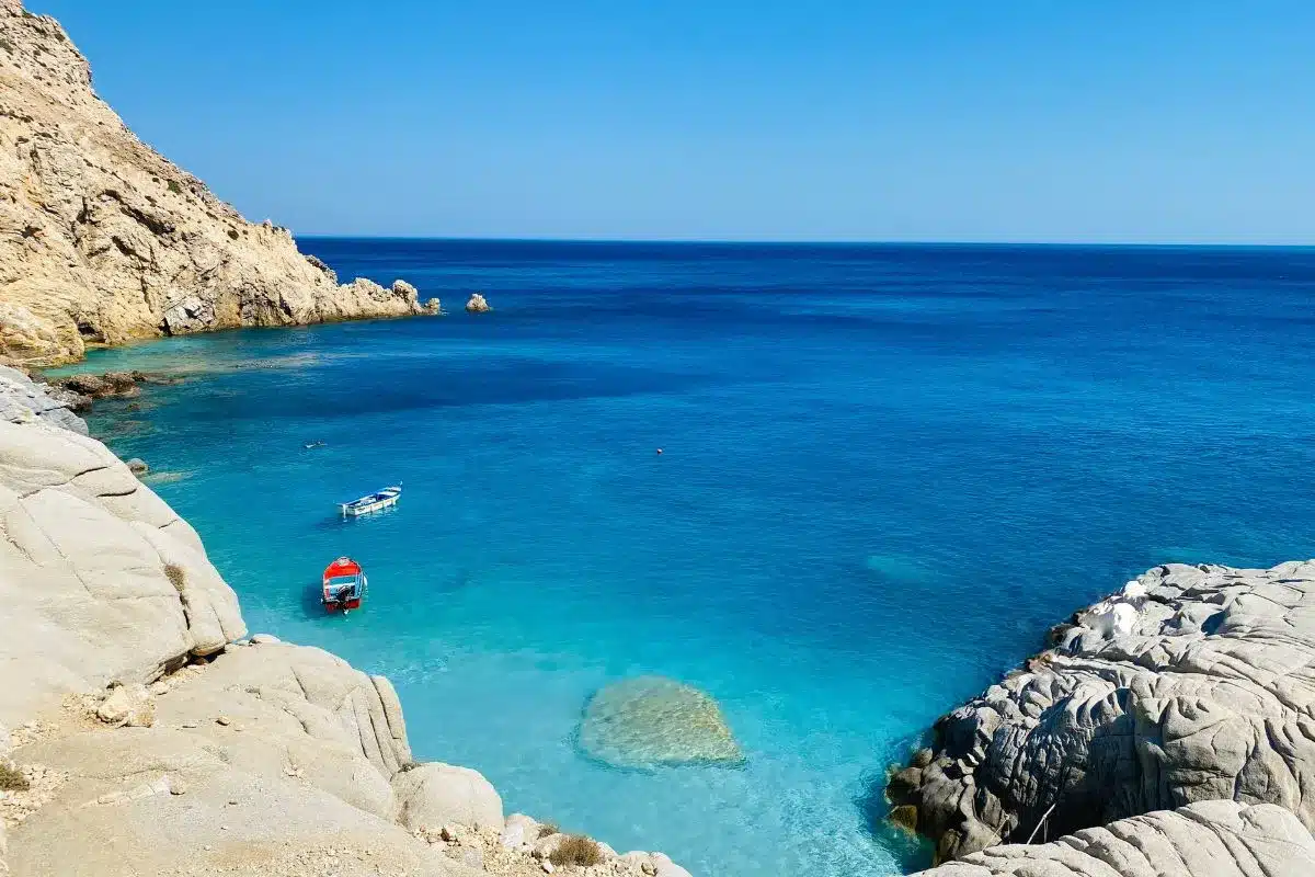 A boat on the coast of an island in blue waters.