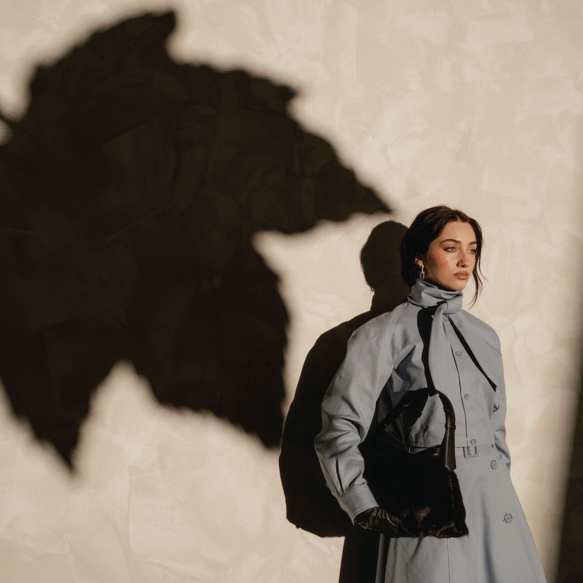 woman dressed in a coat stands against a wall.