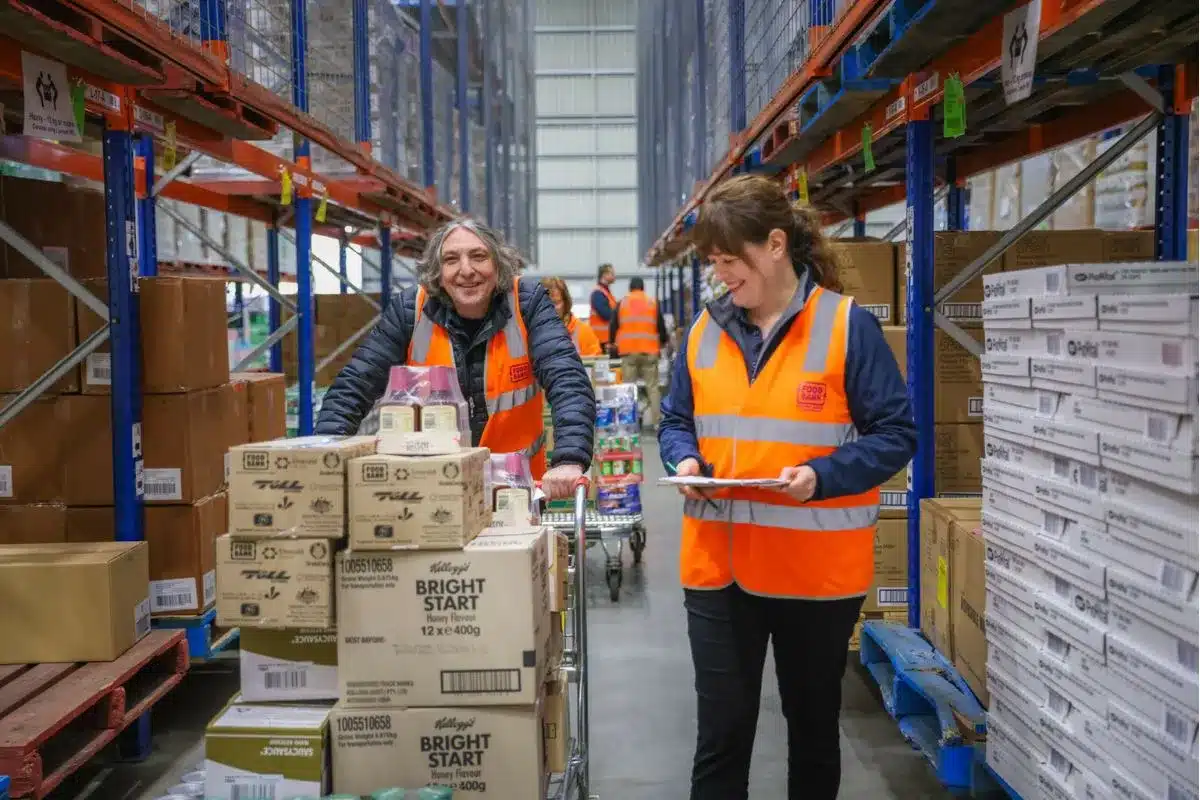 Two people standing in an aisle surrounded by numerous stacked boxes.