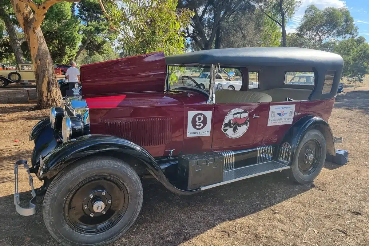 A fully restored burgundy and black 1920s vintage car parked at an outdoor classic car event, displaying Grundy's Shoes and Royal Flying Doctor Service signage on the door.