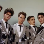 Vintage promotional photo of New Zealand band Split Enz, showing six members in matching grey suits decorated with bold black and white graphic patterns, wearing theatrical makeup.