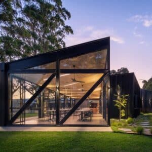 Modern glass-walled pavilion at Anvers Wines in the Adelaide Hills, set among greenery and trees, showcasing contemporary architecture and vineyard surroundings at dusk.