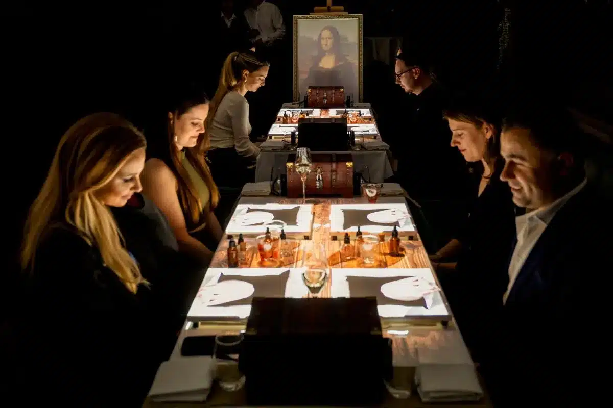 A group of people dining in a restaurant with images projected from above and a variety of vials for a performative meal.