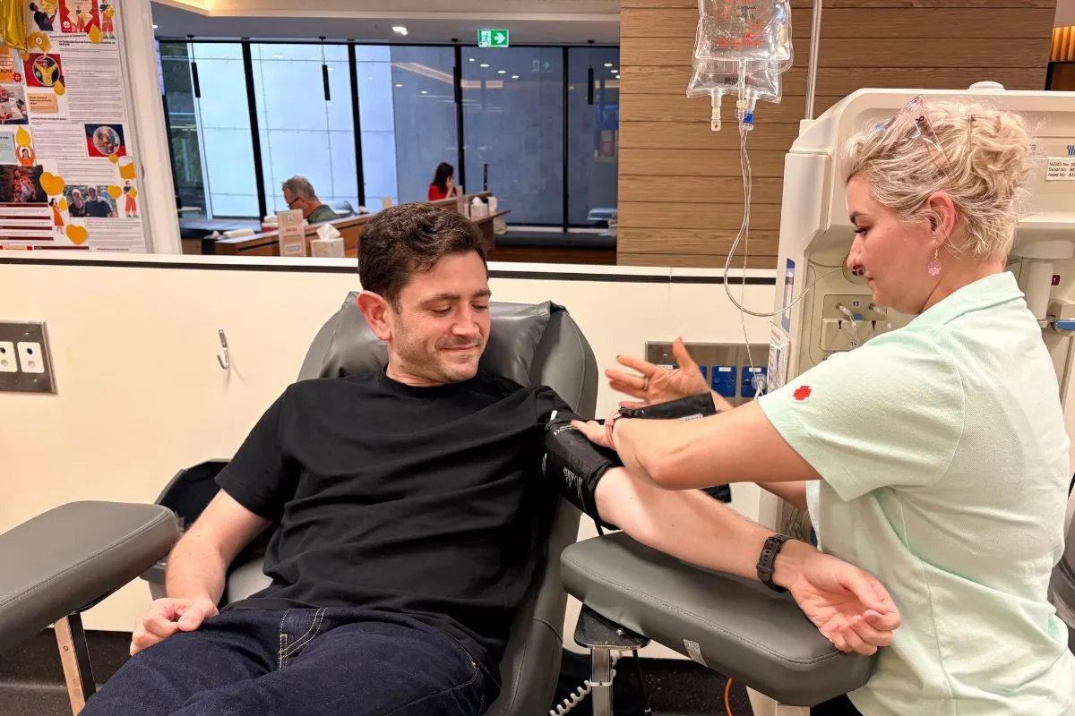 A man laying in chair donating blood being tended to by a nurse in a donation centre.