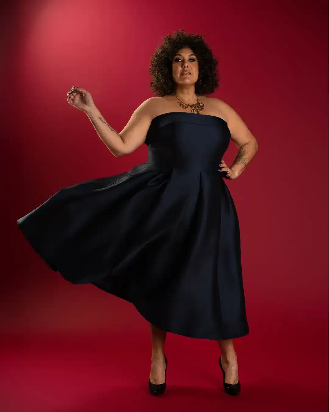 Musician Casey Donovan dressed in a black strapless dress and red necklace against a deep red backdrop.
