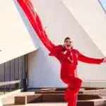 A performer in a flowing red jumpsuit leaps mid-air against a blue sky backdrop during the Adelaide Cabaret Festival.
