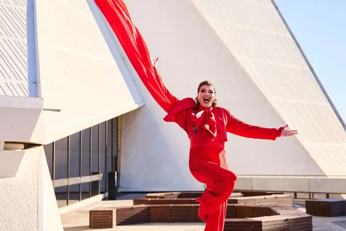 A performer in a flowing red jumpsuit leaps mid-air against a blue sky backdrop during the Adelaide Cabaret Festival.