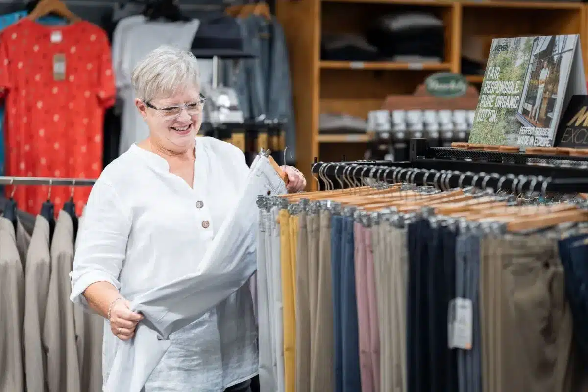 A woman in a white shirt stands beside well-stocked clothing rack displaying a trousers inside Mr Menswear in Victor Harbor.