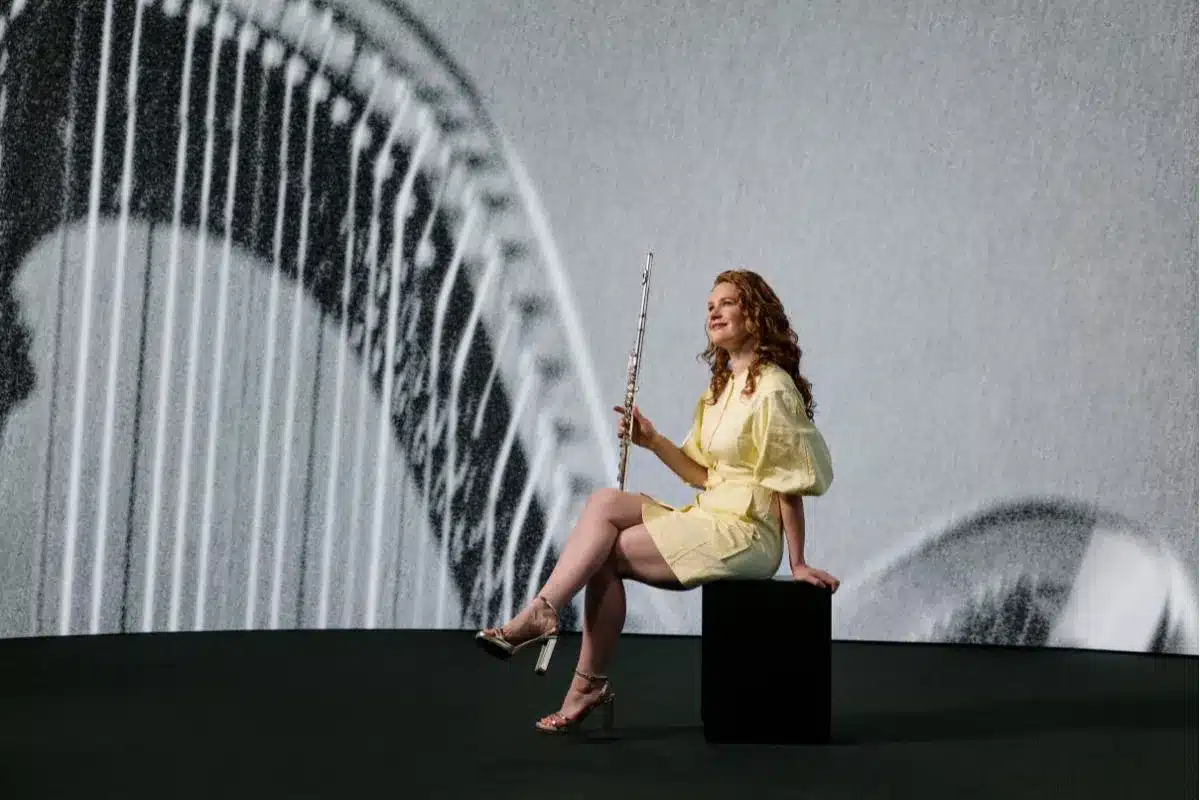 ASO flautist in performance against a harp-themed projection backdrop
