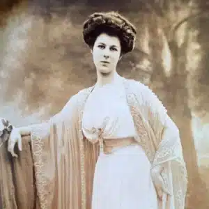 A sepia-toned Edwardian portrait photograph of a young woman in a delicate lace-trimmed gown, her dark hair pinned up in the style of the early 1900s.