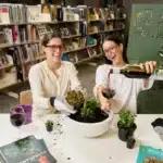 Two women laughing while potting succulents and pouring wine at a South Australian library as part of the Firstival program