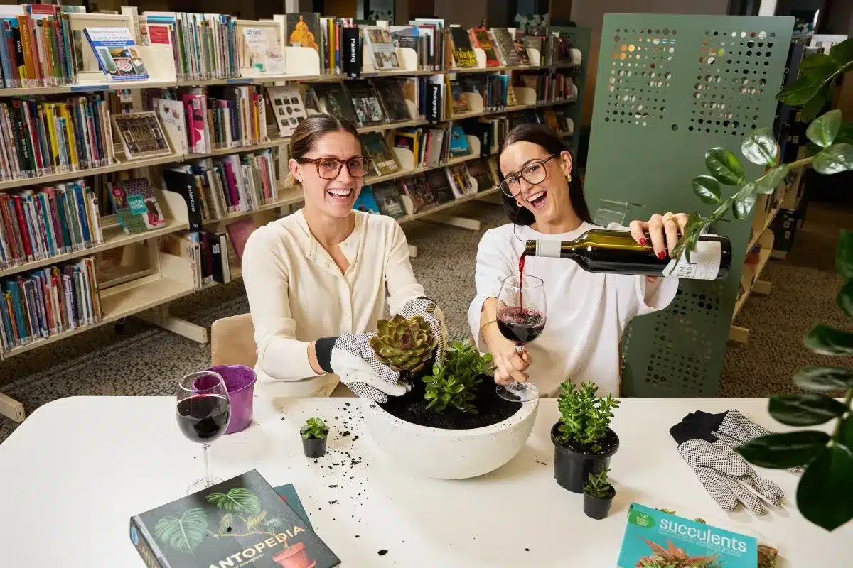 Two women laughing while potting succulents and pouring wine at a South Australian library as part of the Firstival program