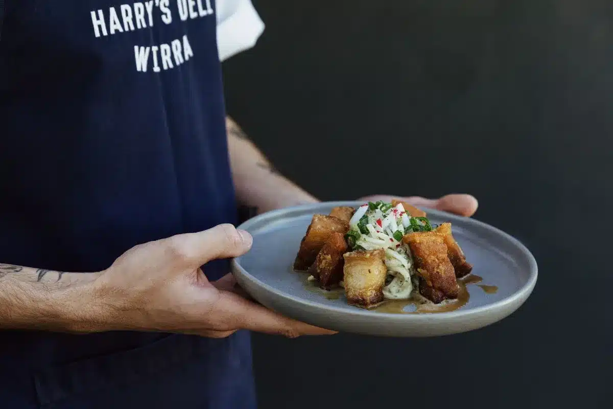A Harry's Deli Wirra Wirra chef holds a plate of food with a golden sauce, from the new winter menu at McLaren Vale