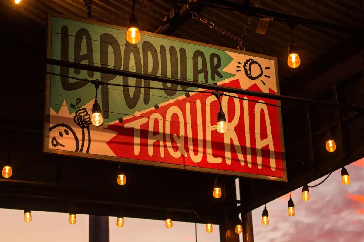 The hand-painted La Popular Taqueria sign illuminated by warm string lights at dusk on St Vincent Street, Port Adelaide