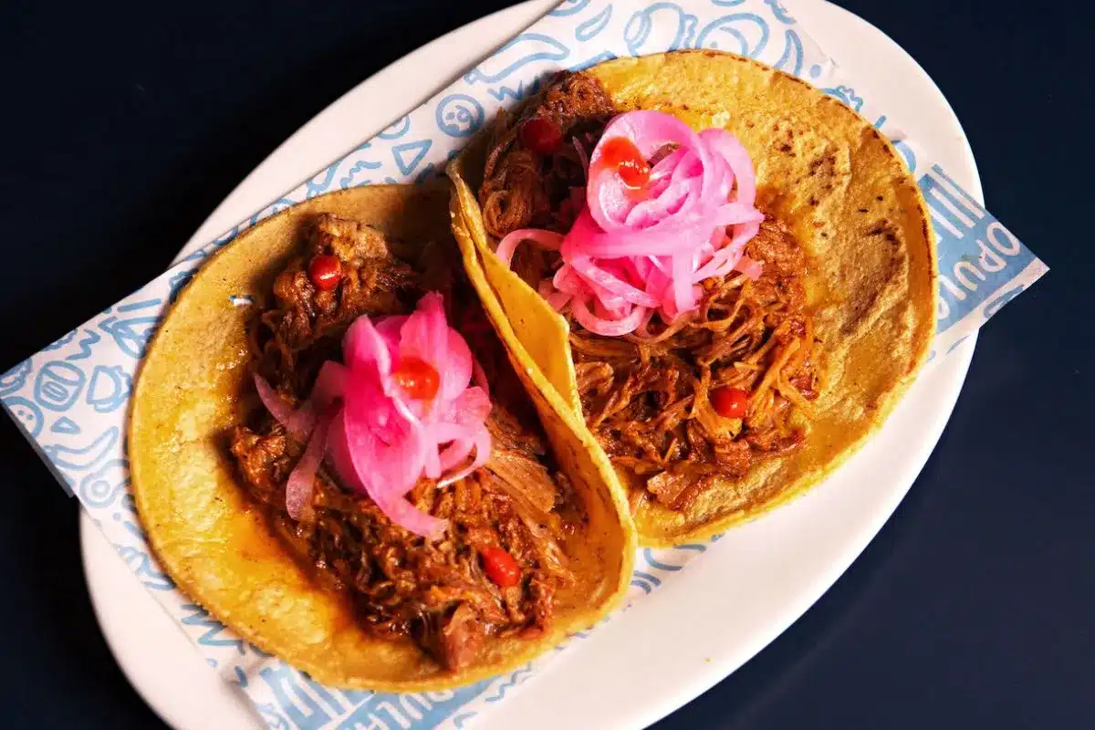 Two Cochinita Pibil tacos on hand-made corn tortillas, topped with bright pink pickled onions, served on a white plate at La Popular Taqueria in Port Adelaide