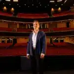 State Opera South Australia artistic director Dane Lam stands on stage at the Adelaide Festival Centre, with the empty red-seated auditorium behind him