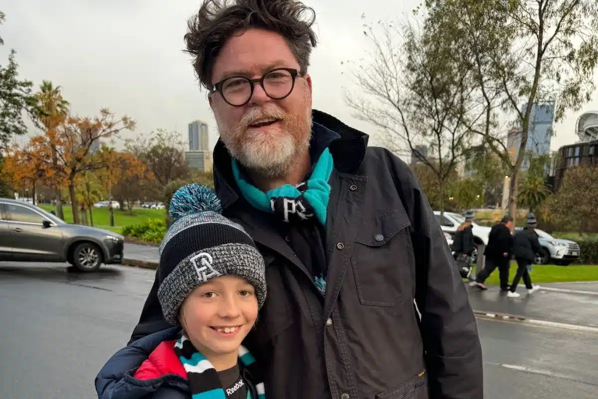 Food and wine writer and Port Adelaide supporter Nick Ryan stands with a young fan in Power colours and scarf on a rainy match day