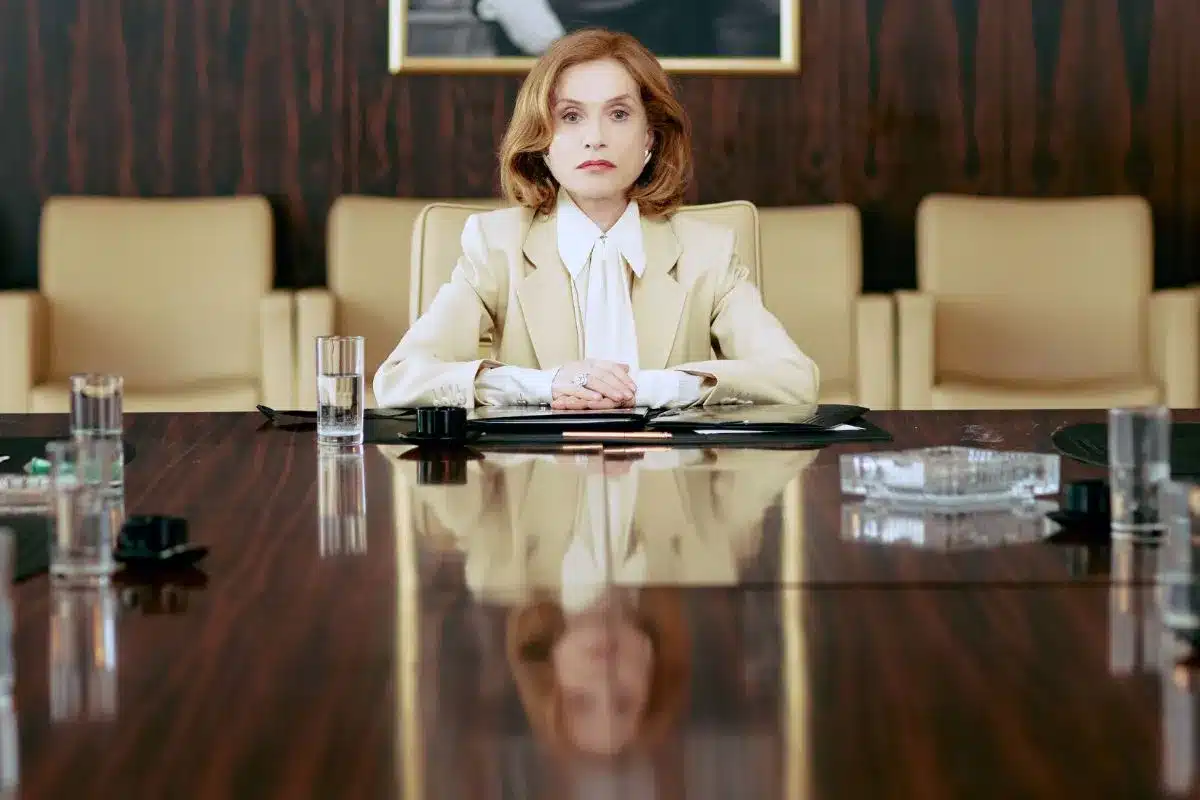 A woman dressed in a business suit sits at the head of a boardroom table in a position of power.