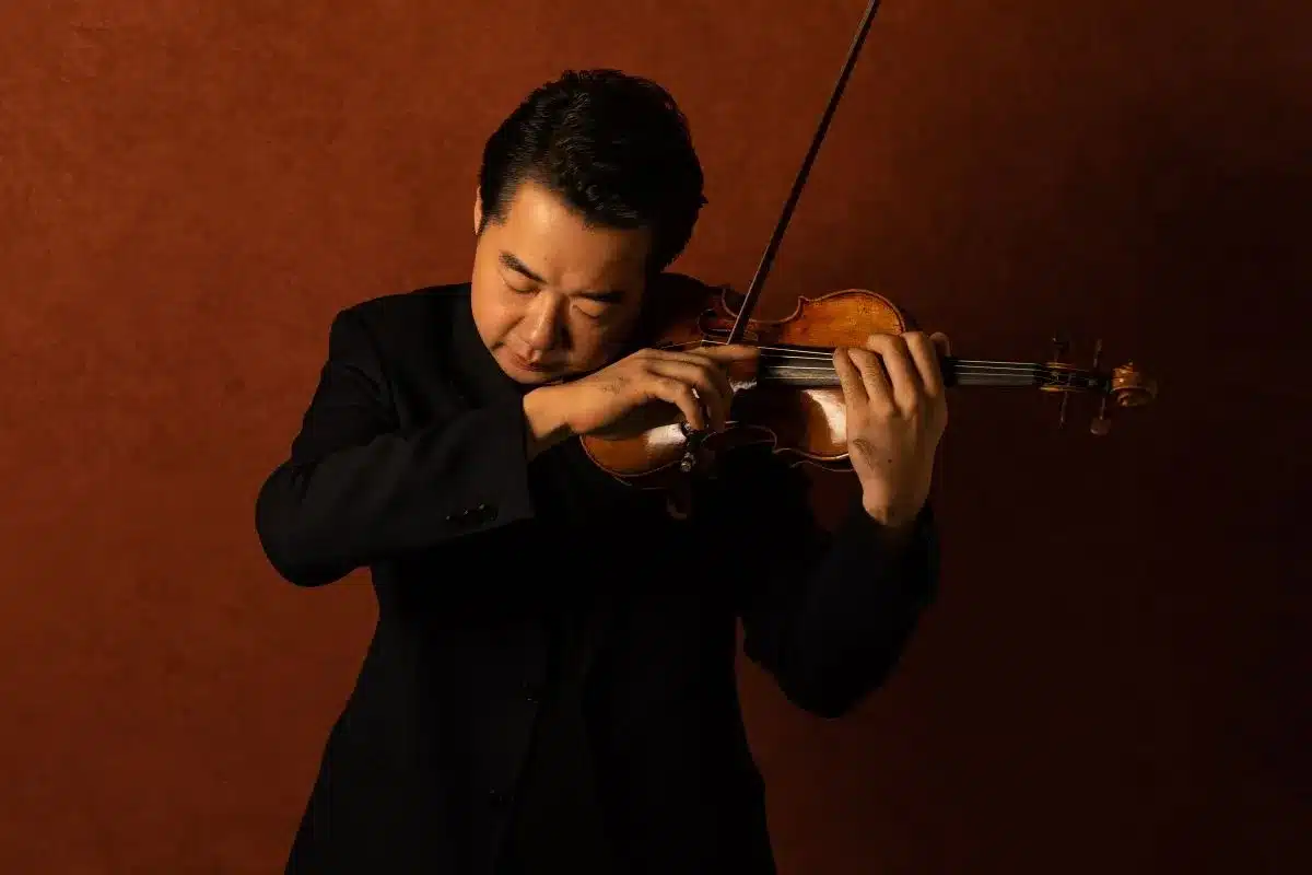 Violinist Ning Feng playing violin against a deep rust-coloured background.