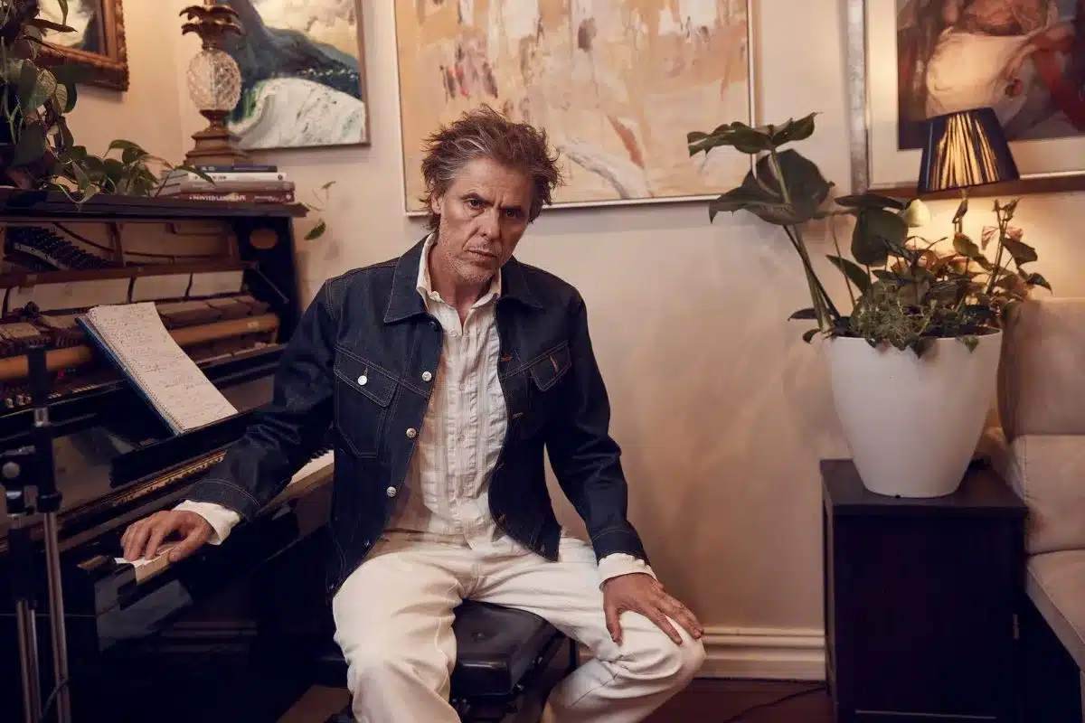 Tim Freedman seated at a piano in a warmly lit room surrounded by artwork and plants