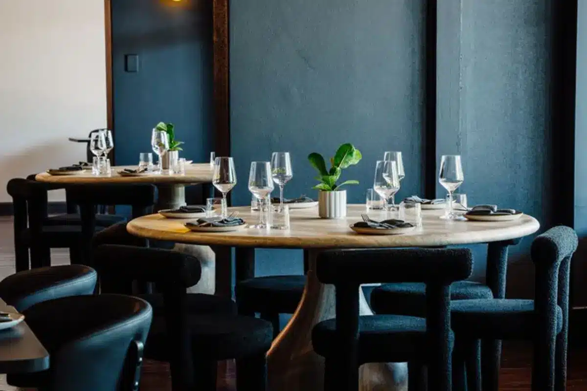 The dark-walled dining room with round timber tables at OZIN restaurant, Adelaide